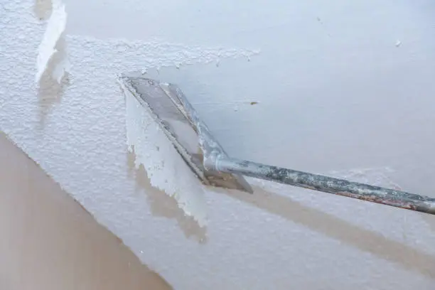 Removing popcorn ceiling texture with a scraping tool during renovation by a painting company in San Carlos, CA.